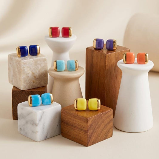 Colorful ceramic square stud earrings displayed on wooden and marble stands against a neutral background