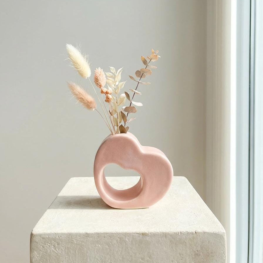 Sculptural pink ceramic vase with dried flowers on a light surface against a neutral wall