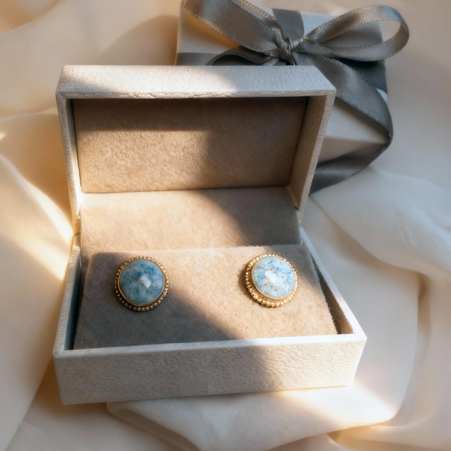 Pair of earrings in a decorative box with a ribbon on a soft fabric background