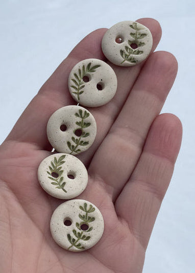 Five ceramic buttons with leaf patterns held in a hand against a snowy background